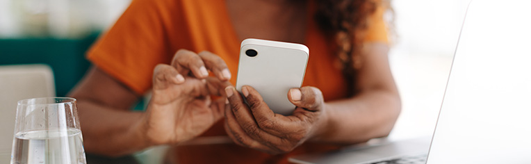 Woman wearing an orange shirt using a cell phone next to an open laptop Woman wearing an orange shirt using a cell phone next to an open laptop