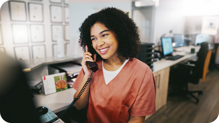 Nurse wearing orange scrubs smiling while on the phone