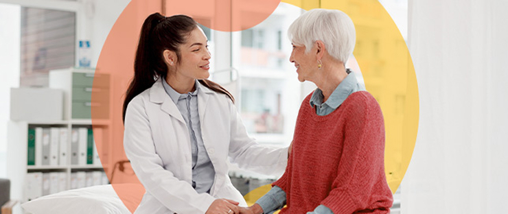 Female doctor sitting next to older female patient on exam table