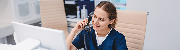 Young female nurse in blue scrubs sitting at a desk on the phone