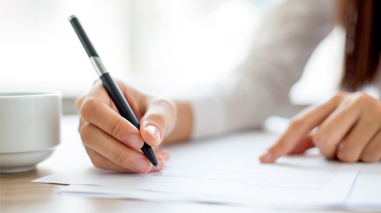 Person signing document on table next to coffee cup