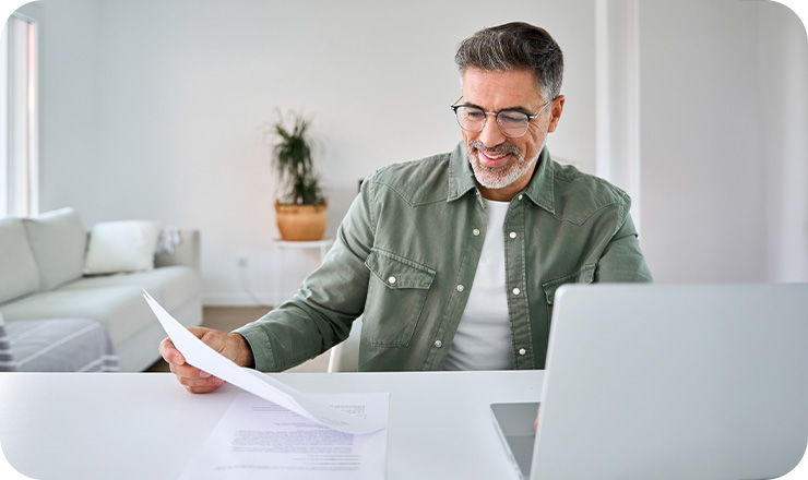Man wearing a green shirt smiling while holding a document next to his laptop