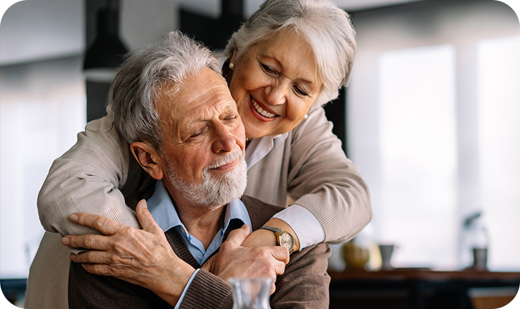 Smiling older woman with her arms around an older man sitting in front of her