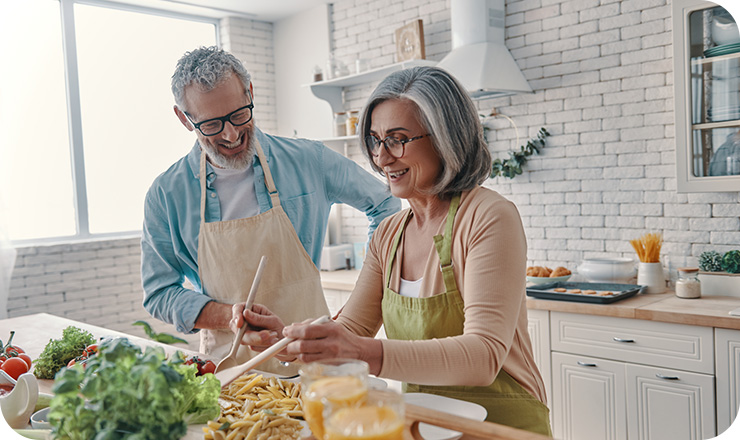 Older couple laughing together as they prepare food in a kitchen