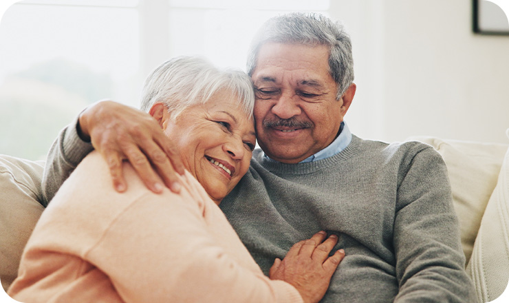 Smiling older couple embracing on a white couch in a living room