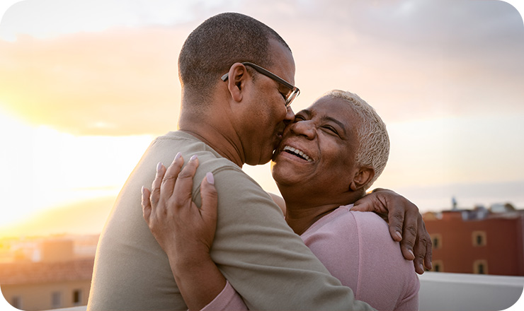 Older man and woman hugging outside in front of a sunset