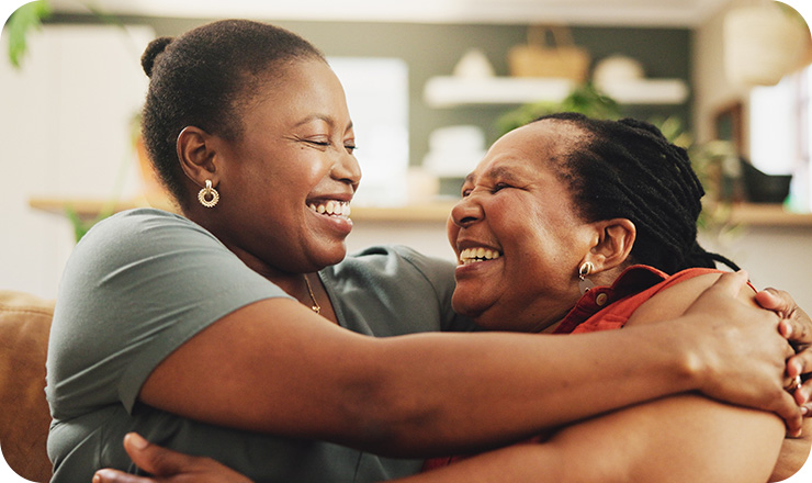 Older mother and daughter smiling at each other and embracing while sitting on a couch
