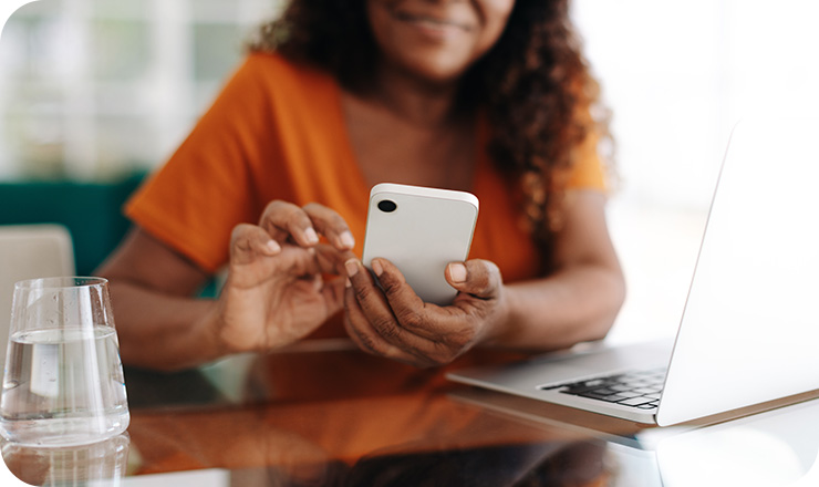 Woman wearing an orange shirt using a cell phone next to an open laptop